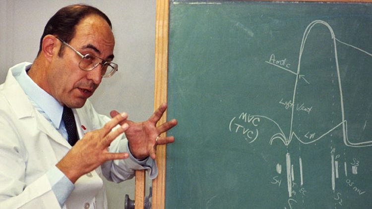 Doctor in white coat gesturing with hands in front of chalk board with auscultation diagram